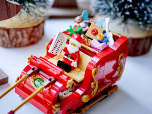 Toy sleigh with Santa Claus figure and Christmas decorations on a white surface.