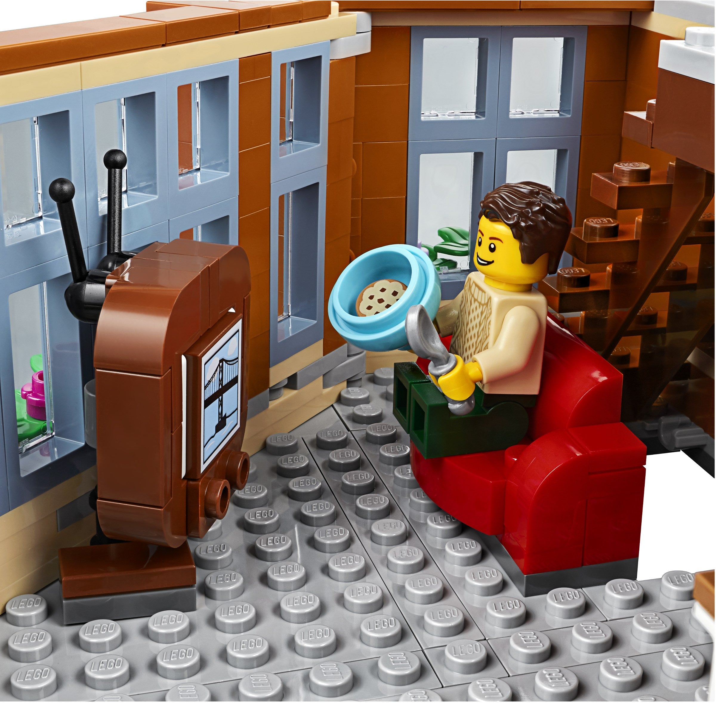 LEGO figure sitting on a red couch with a TV and cookie in a blue bowl.