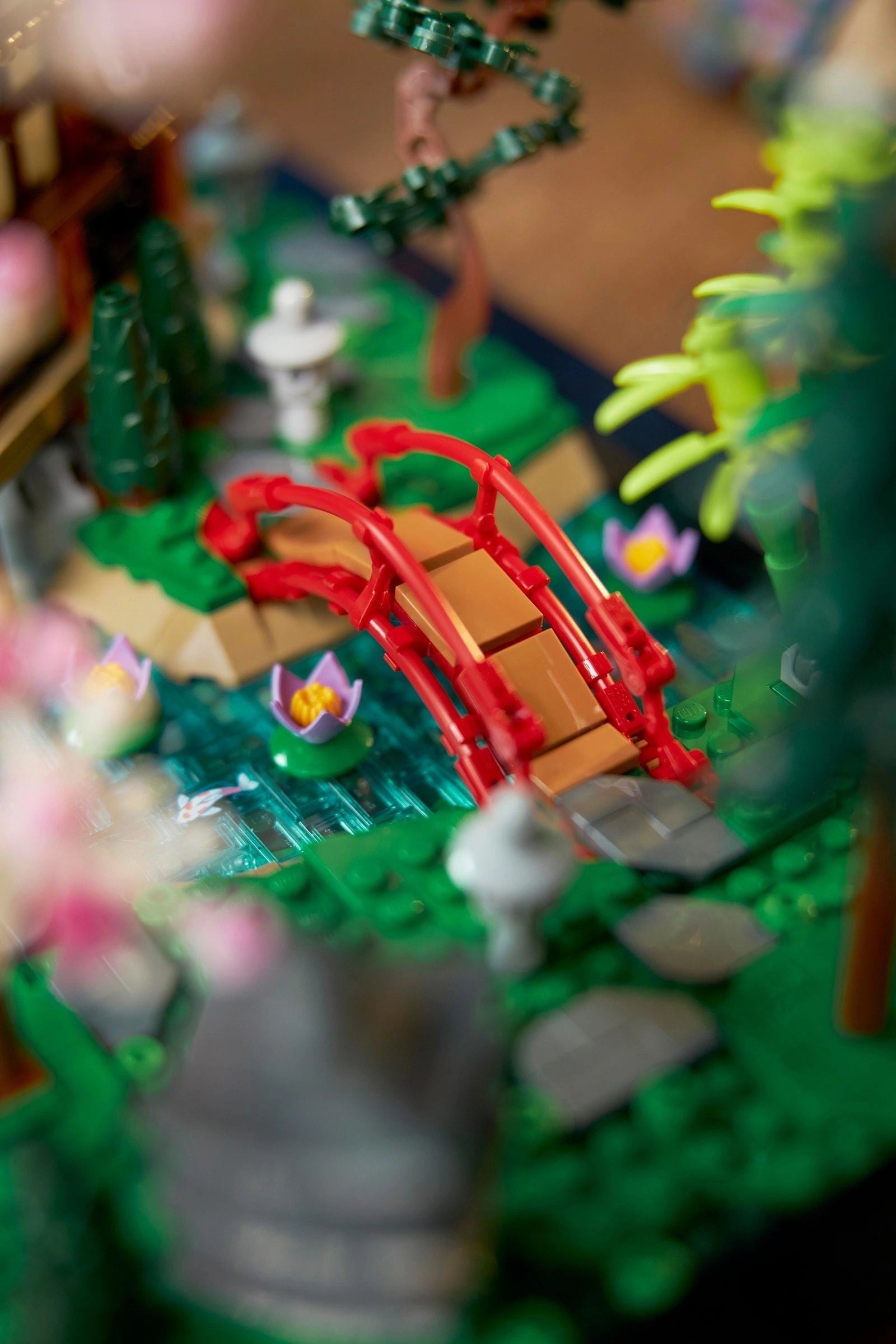 Close-up of a LEGO model with a red bridge, green trees, and small figures on a blurred background.