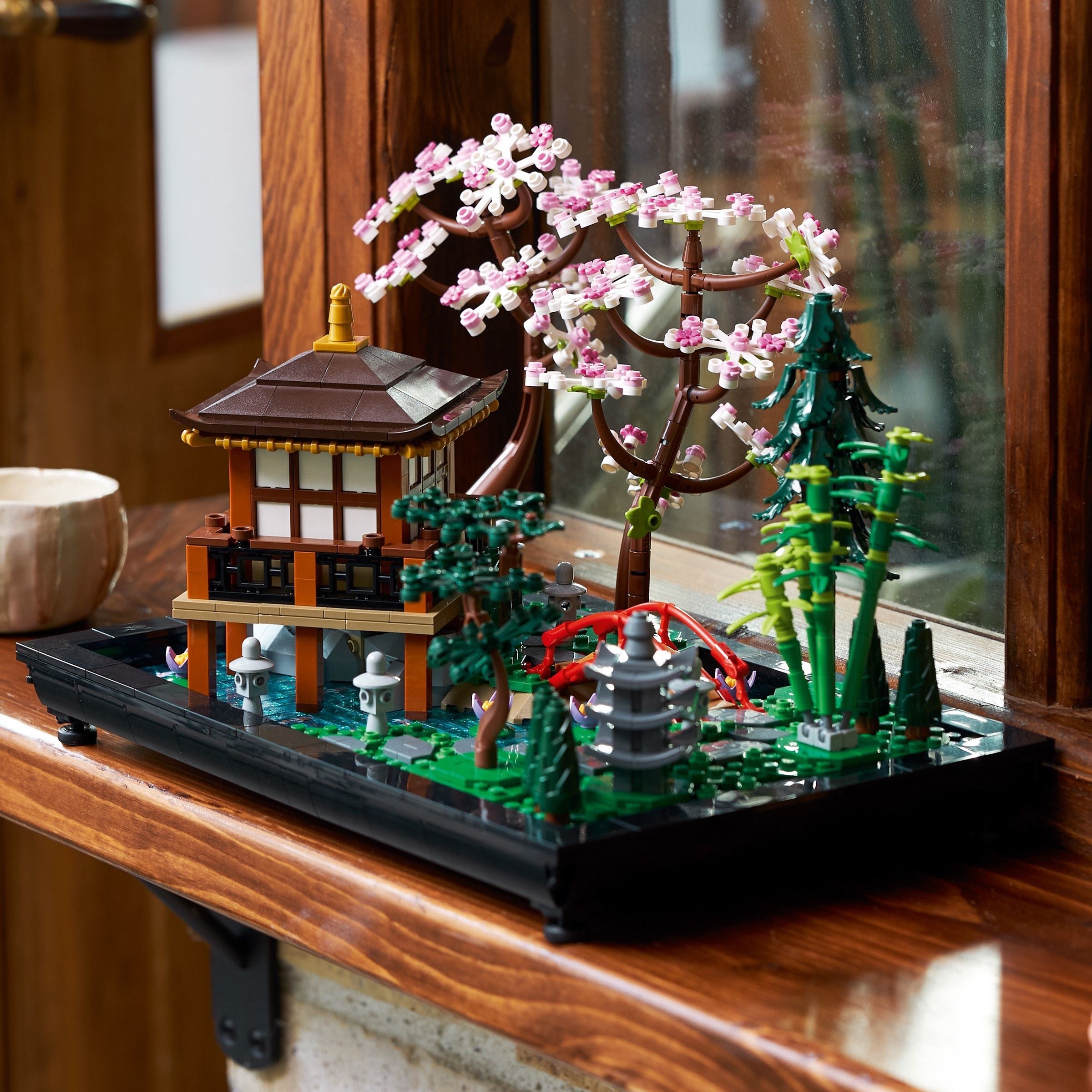 LEGO model of a Japanese temple with cherry blossom tree and fountain on a wooden surface.