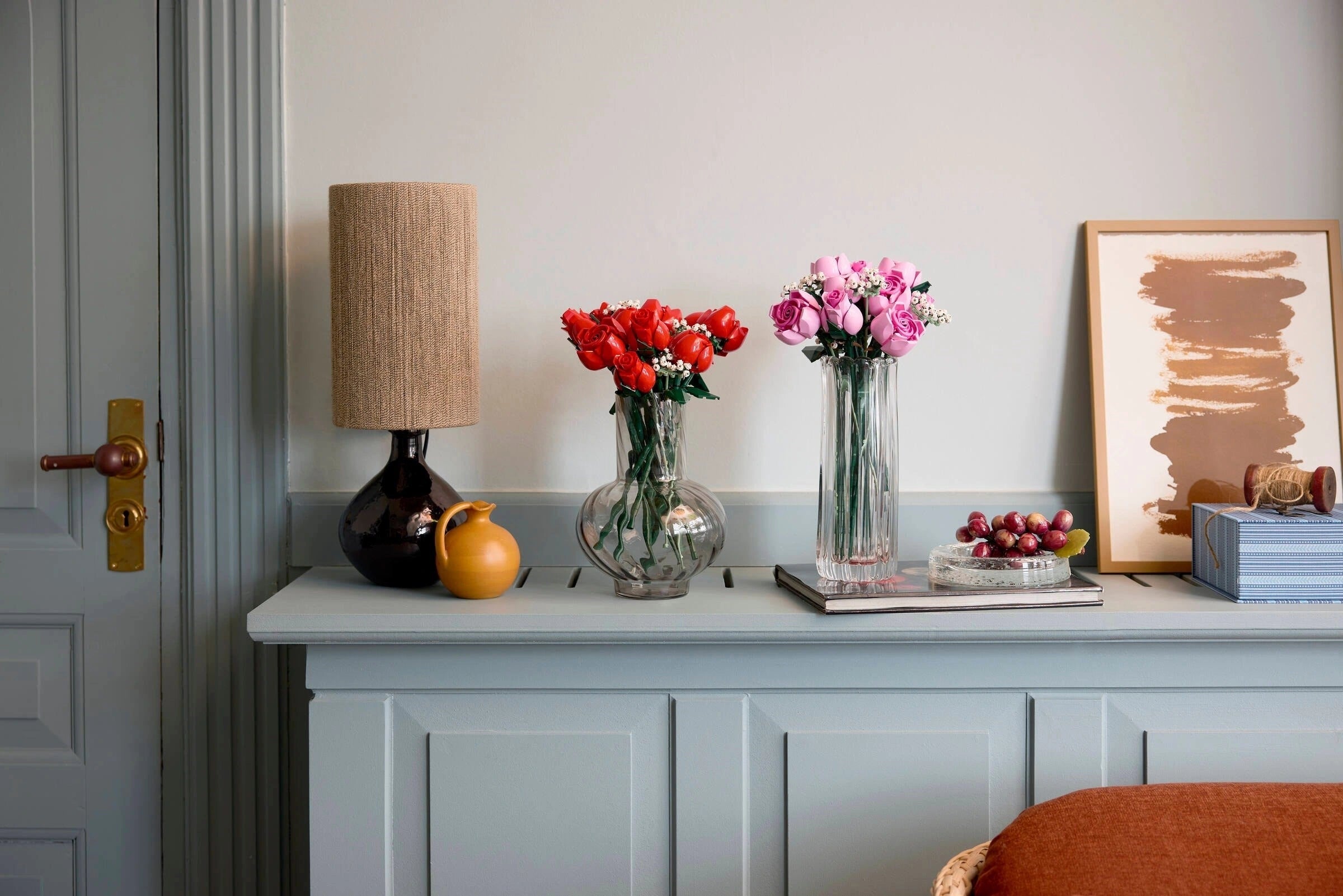 Decorative setup with vases, flowers, and a lamp on a shelf against a light gray wall.