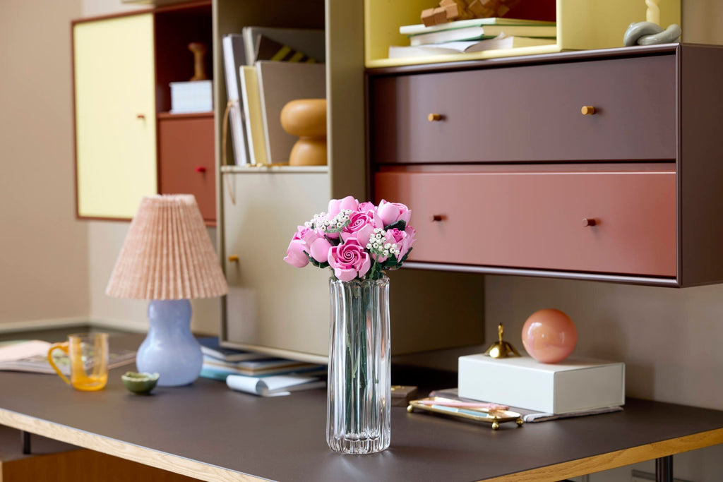 Desk with a vase of pink flowers, lamp, and books in a home office setting.