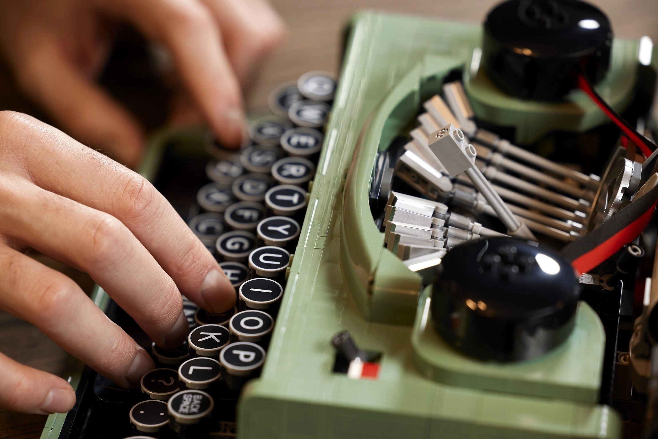 Person typing on a vintage green typewriter with close-up focus on hands and keys.