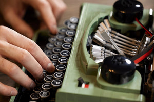 Person typing on a vintage green typewriter with close-up focus on hands and keys.