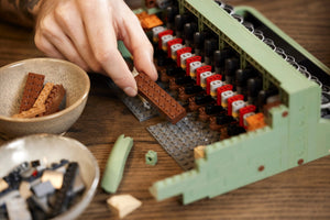 Hand building a lego model on a wooden table with ingredients nearby