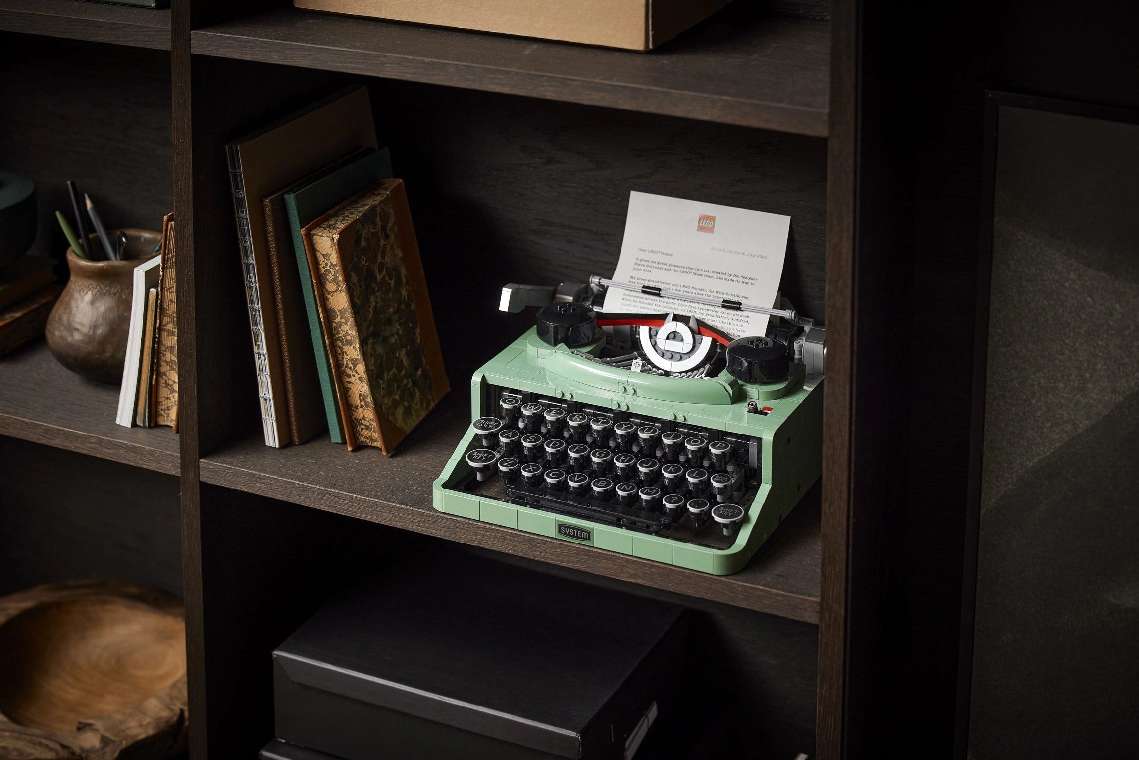 Vintage-style green typewriter on a wooden shelf with books and a box.