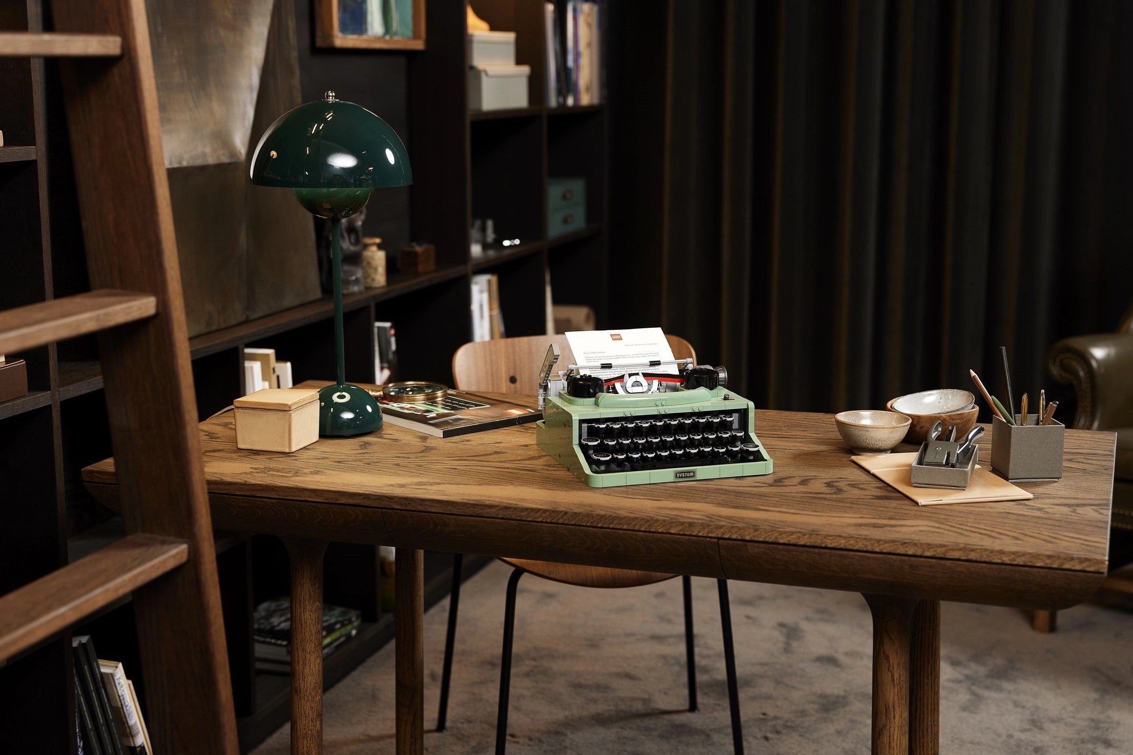 Vintage green typewriter on a wooden desk with bookshelves and decor in the background
